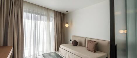 A modern living room with a sofa, a coffee table, and a large window with curtains.