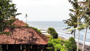 A beachfront property with a thatched-roof structure, a patio, and lush greenery. - A hidden gem, away from the hustle and bustle of everyday life. (Karangasem)