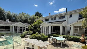 A spacious outdoor patio with a pool, a dining area with a table and chairs, and a large house with multiple windows and a tiled roof. - Templestowe Luxe Retreat | Pool, Tennis Court & Private Oasis (Templestowe)