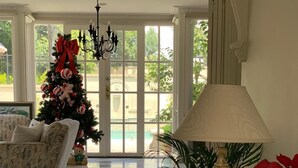 A spacious living room with a large window, a Christmas tree, a sofa, and a dining area with a lamp and a glass table. - Templestowe Luxe Retreat | Pool, Tennis Court & Private Oasis (Templestowe)