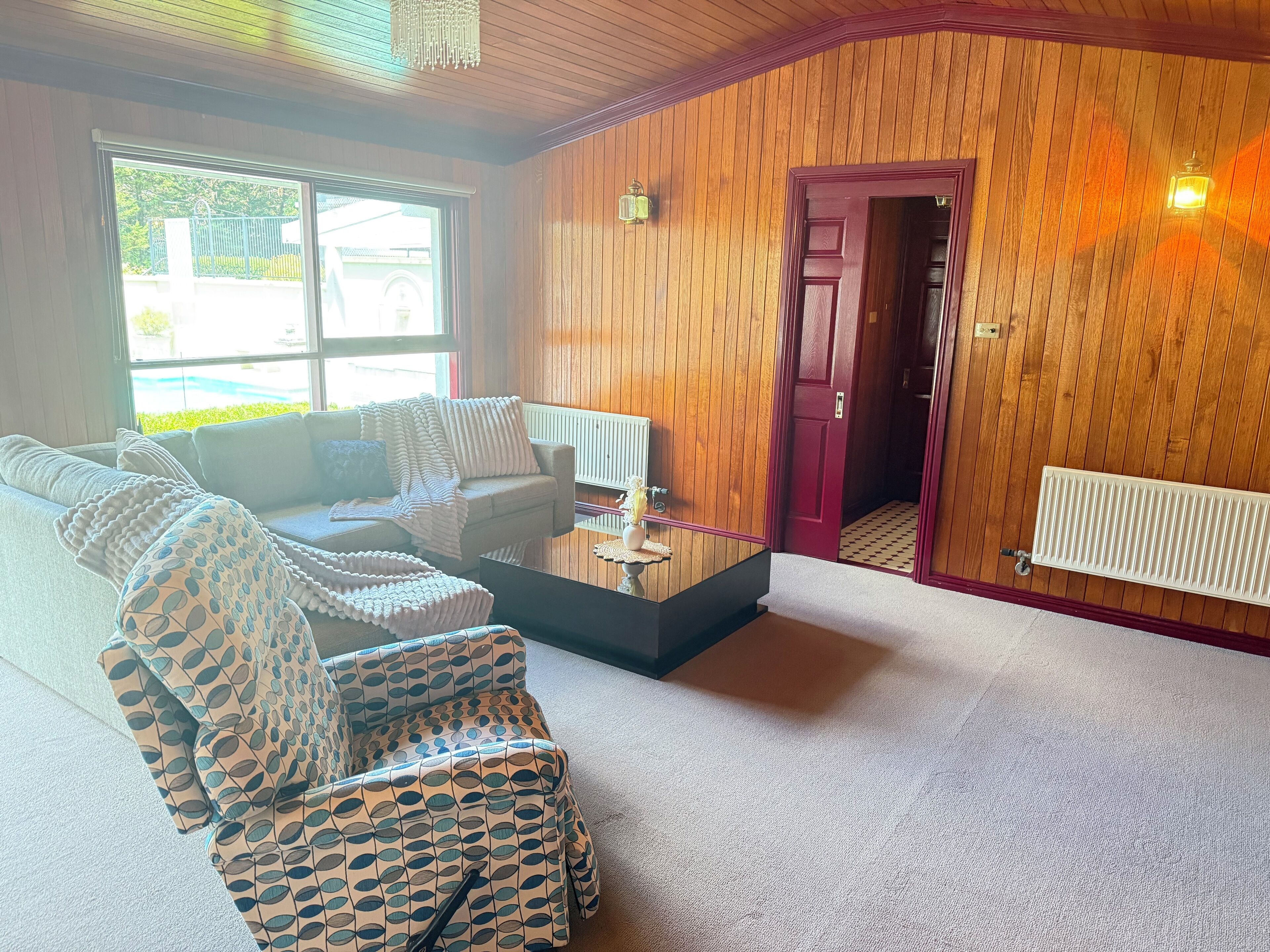 Uma sala de estar com sofá, poltronas estampadas, mesa de centro e parede de madeira com porta.