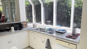 A kitchen with white cabinets, a stainless steel sink, a dish rack, and a window overlooking greenery. - Templestowe Luxe Retreat | Pool, Tennis Court & Private Oasis (Templestowe)