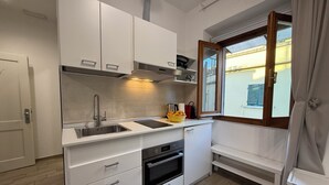 Une cuisine moderne avec des meubles blancs, un évier en acier inoxydable, un four et une fenêtre donnant sur un bâtiment à l’extérieur.