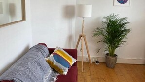 Una habitación con un sofá rojo, una lámpara de pie, una planta en maceta y una obra de arte enmarcada en la pared.
