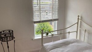 Una cama de metal blanca en una habitación con ventana y una mesita de metal.