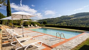A pool area with lounge chairs and umbrellas, surrounded by stone tiles and a view of rolling hills. - My Exclusive Italy - Authentic Chianti's Villa with Private Pool and view (Panzano In Chianti)