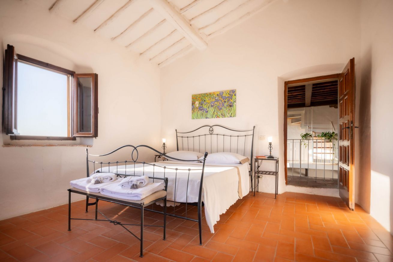A bedroom with a metal bed frame, a window, a painting on the wall, and a balcony door.