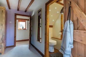 Un pasillo que conduce a un baño con puerta de madera, un espejo y una toalla colgada en un perchero.