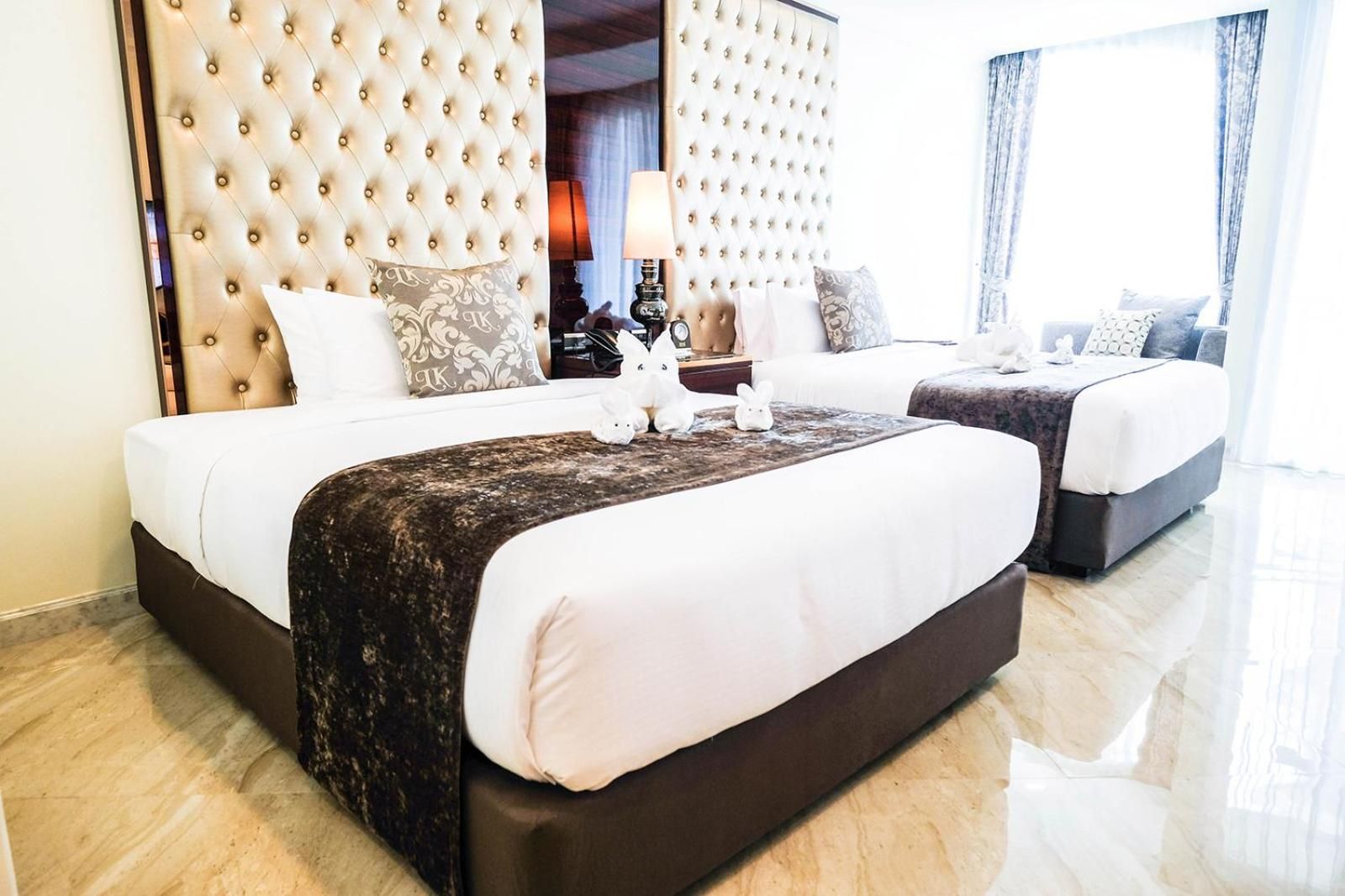 A hotel room with two beds, a tufted headboard, and a nightstand with a lamp.