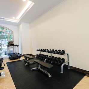 A gym with a treadmill, bench, and dumbbells.