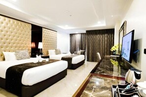 Une chambre d’hôtel avec un grand lit, un plus petit lit, un bureau avec une chaise, une télévision et un vase décoratif.