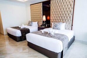 A hotel room with two beds, a large padded headboard, a nightstand, and a lamp. - LK Grand Empire (Pattaya)