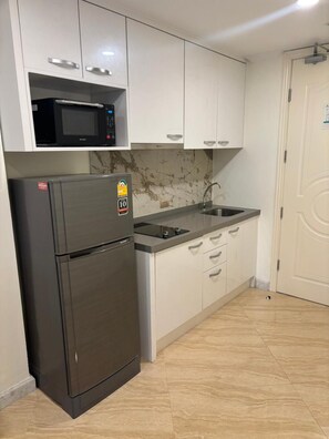 A kitchen with white cabinets, a black refrigerator, a microwave, and a sink.