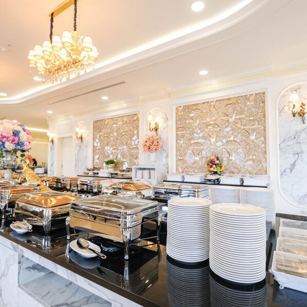 A buffet setup with multiple serving stations, a chandelier, and decorative wall panels. - LK Grand Empire (Pattaya)