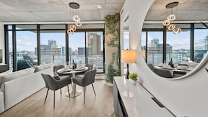 A modern living room with a dining area, large windows, and a city view.