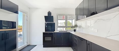 A modern kitchen with black cabinets, a white countertop, and a view of the outdoors.