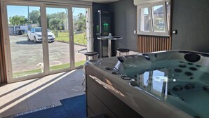 Une salle de spa équipée d’un jacuzzi, d’une petite table avec une chaise et d’une fenêtre donnant sur un parking.