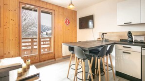 Eine gemütliche Küche mit Holzwänden, einem großen Fenster mit Blick auf schneebedeckte Berge, einer Bar mit Hockern und einer modernen Kaffeemaschine.