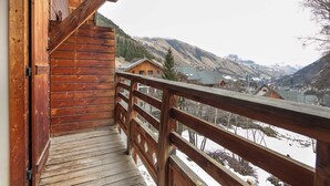 Eine Holztreppe führt zu einem Balkon mit Blick auf eine verschneite Berglandschaft und ein Dorf darunter.