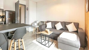 Ein modernes Wohnzimmer mit grauem Sofa, einem Couchtisch und einer Küchenzeile mit Kühlschrank.