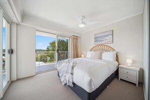 Ein Schlafzimmer mit einem großen Bett, einem Deckenventilator, einem Nachttisch und Blick ins Freie durch eine Schiebetür.