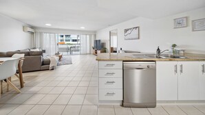 A modern kitchen with white cabinets, a stainless steel dishwasher, and a large island with a sink.