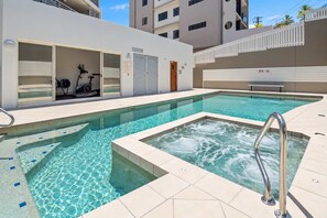 Een zwembad met een jacuzzi, een overdekte fitnessruimte en een witte schutting.