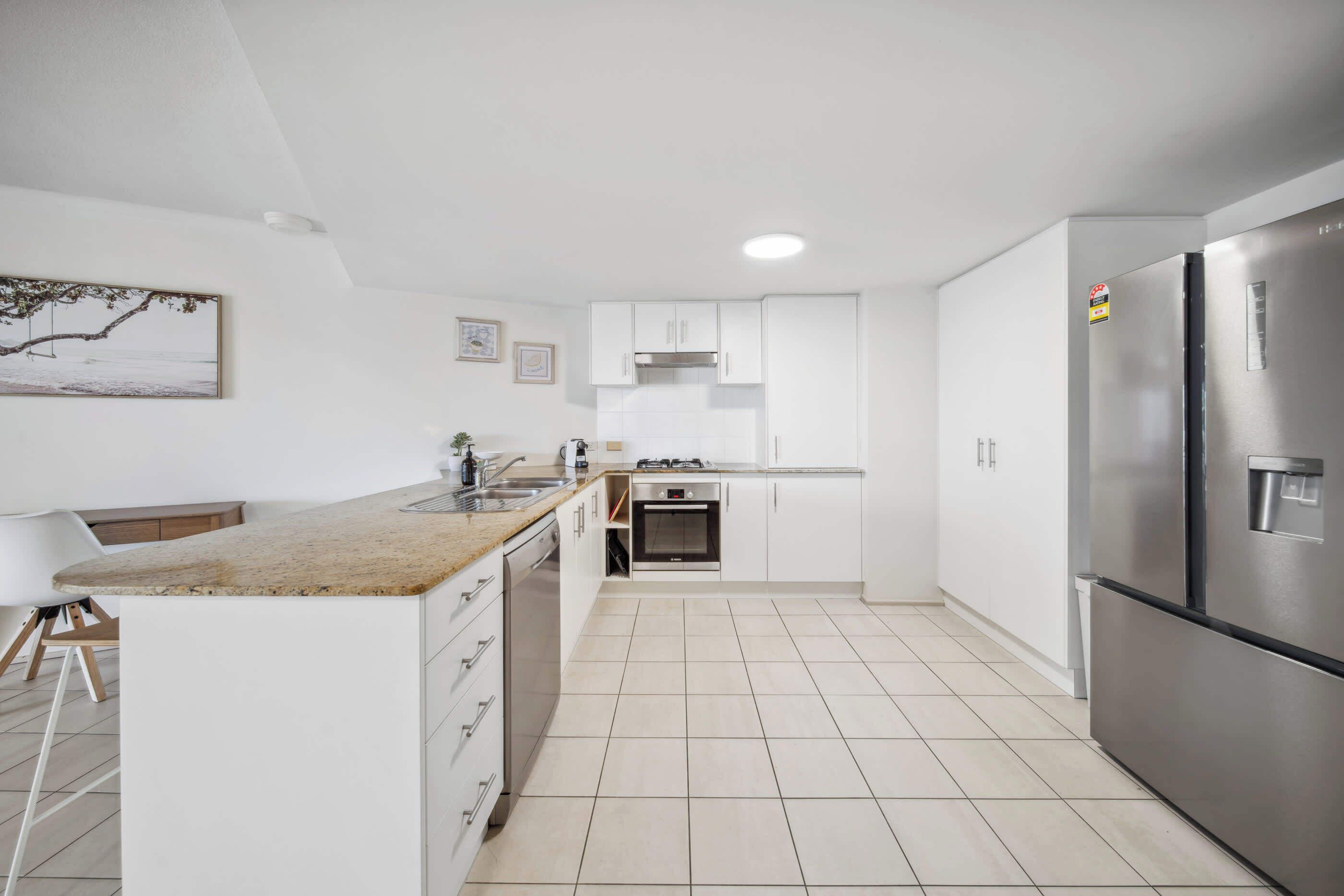A modern kitchen with white cabinetry, a stainless steel refrigerator, and a tiled floor.