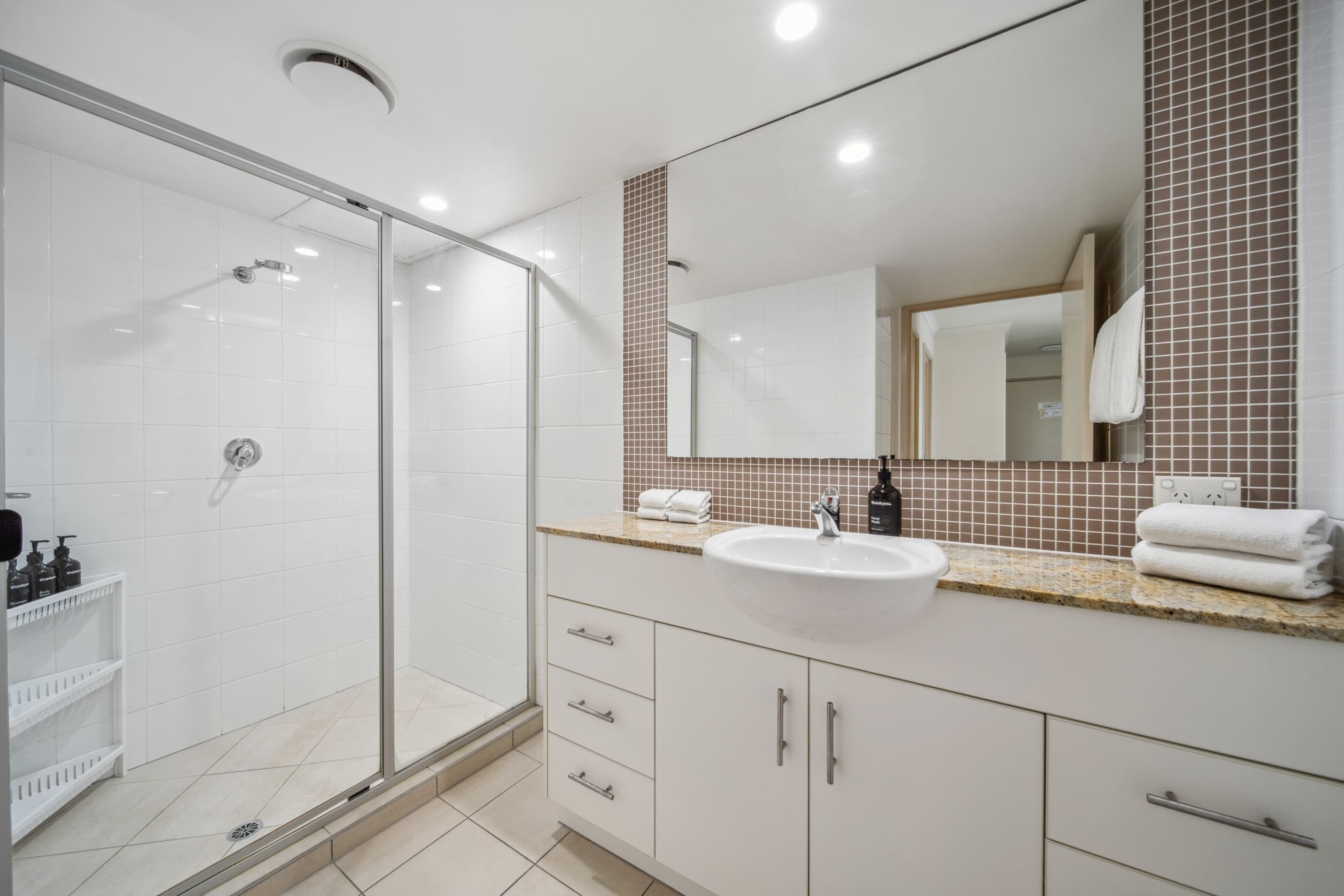A modern bathroom with a glass shower enclosure, a white sink, and a large mirror.