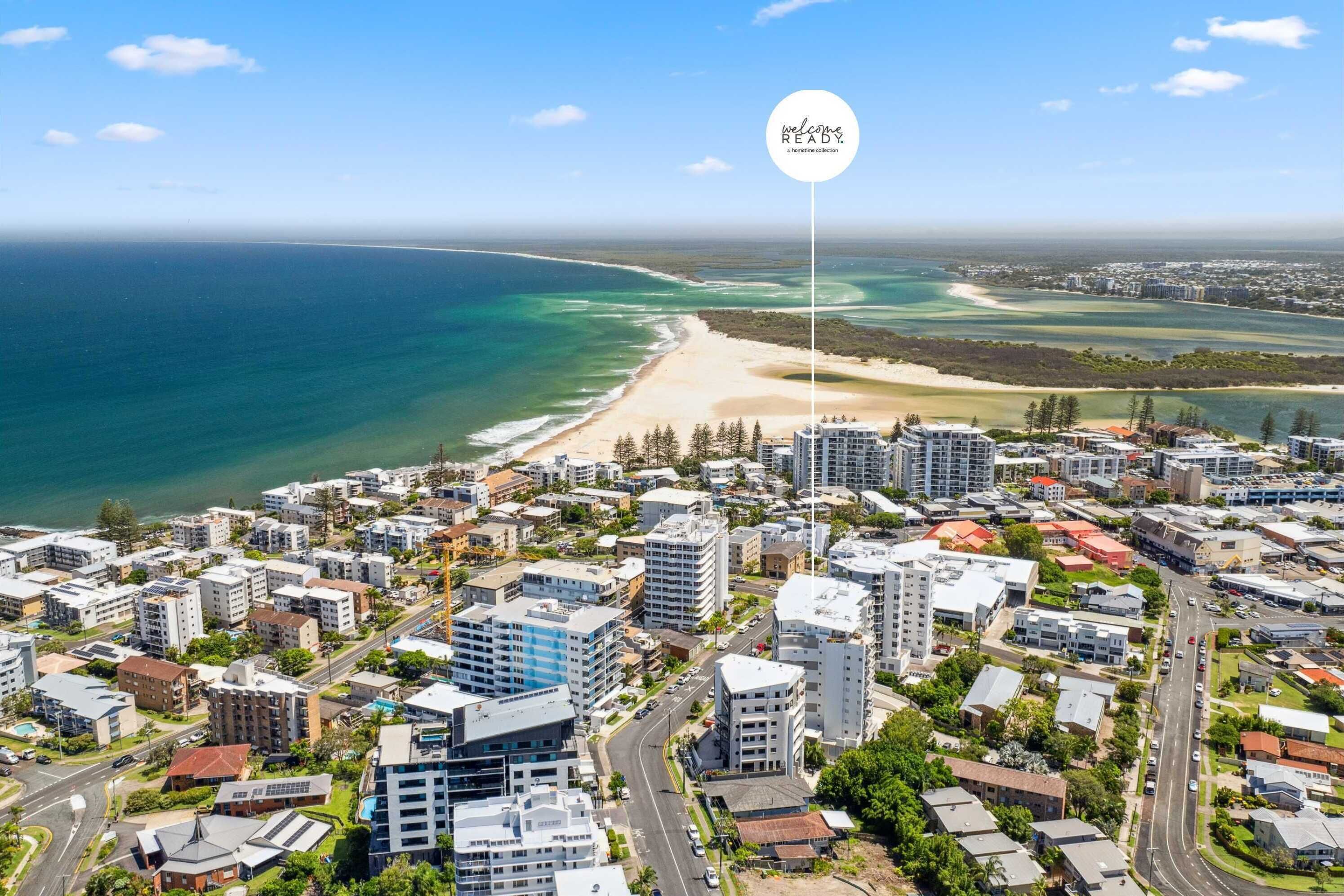 An aerial view of a coastal city with a beachfront, high-rise buildings, and a clear sky.
