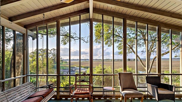 A covered porch with a wooden bench, two wicker chairs, and a small round table. - Hot Tub & Grill | Folly Marsh House (Folly Beach)