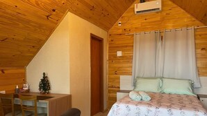 Una habitación acogedora con techo de madera, una cama con ropa de cama estampada con flores, un escritorio pequeño con una silla y un árbol de Navidad.