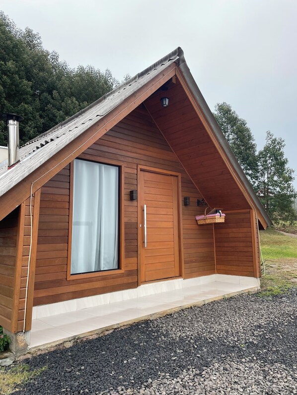 Una cabaña de madera con techo a dos aguas, un ventanal grande y una puerta.