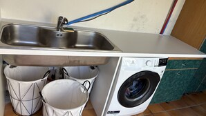 A compact kitchen with a stainless steel sink, a washing machine, and two white laundry baskets. - Studio Azur et Mer tout CONFORT (Dolus-d'Oléron)