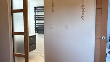 A room with a bed, a bench, a wooden door, and a wall with two electrical outlets.
