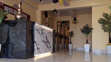 A hotel lobby with a marble reception desk, ceiling fans, chandeliers, and potted plants.