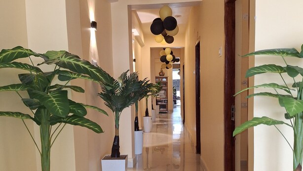 A hallway with potted plants, a light-colored floor, and ceiling decorations. - Hotel Grand Arya (Hilsa)