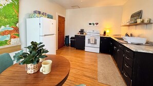 A compact kitchen with a refrigerator, stove, and sink. There's a wooden dining table with chairs and a potted plant. - A Charming Door County Condo in the heart of Sturgeon Bay (Sturgeon Bay)