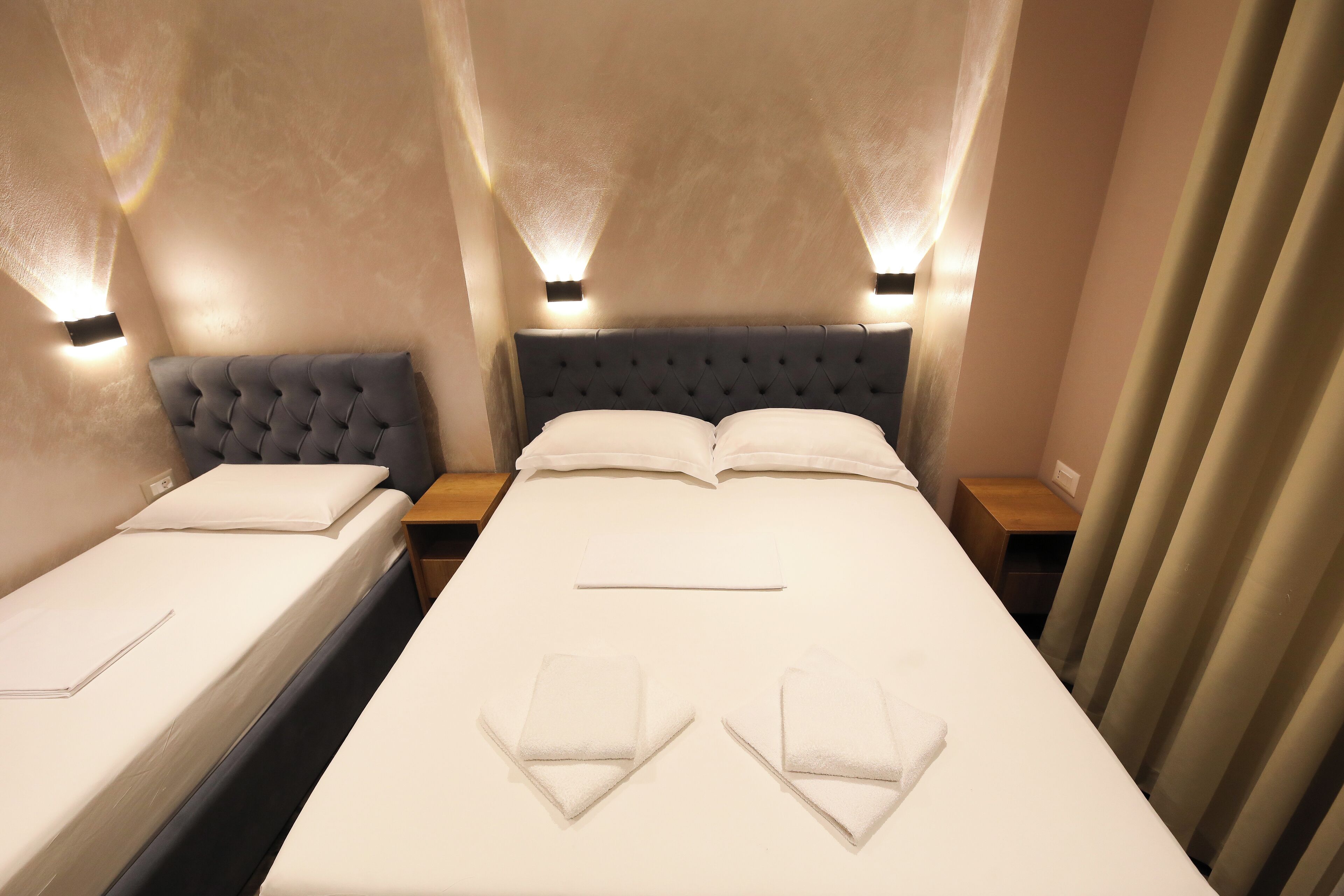 A hotel room with two beds, a tufted headboard, bedside lamps, and neatly folded towels.