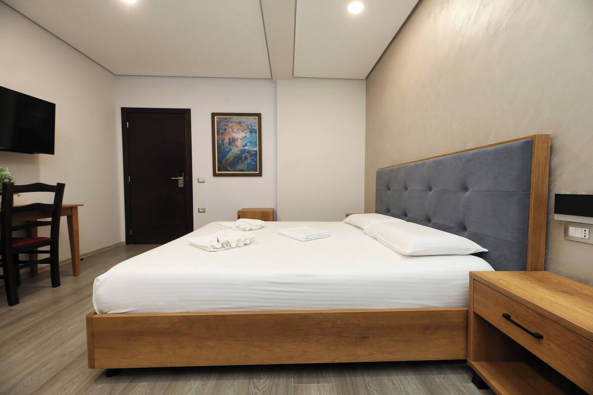 Une chambre bien rangée, avec un lit, une table de chevet et un téléviseur fixé au mur.