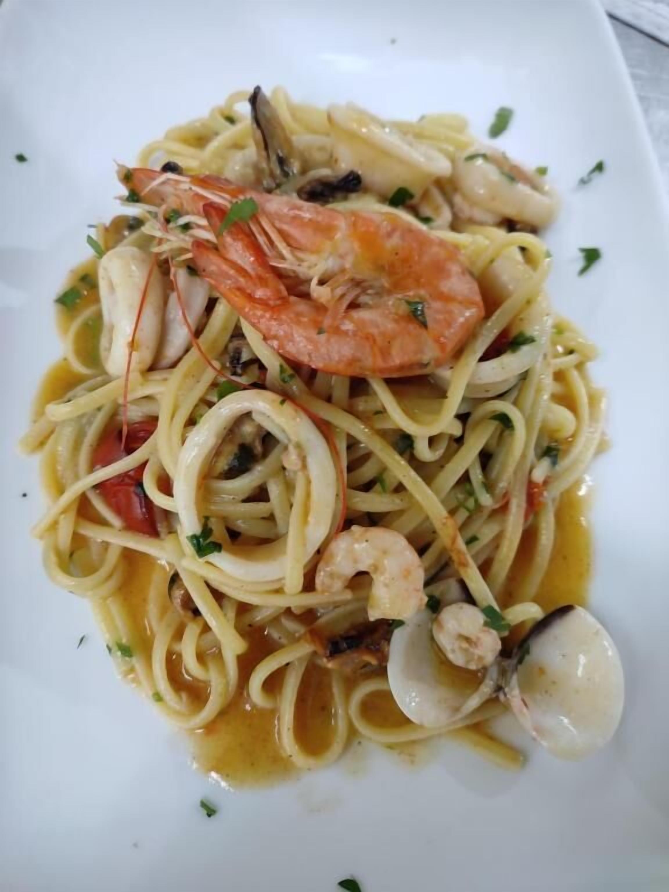 Un plato de pasta con camarones, almejas y salsa cremosa.