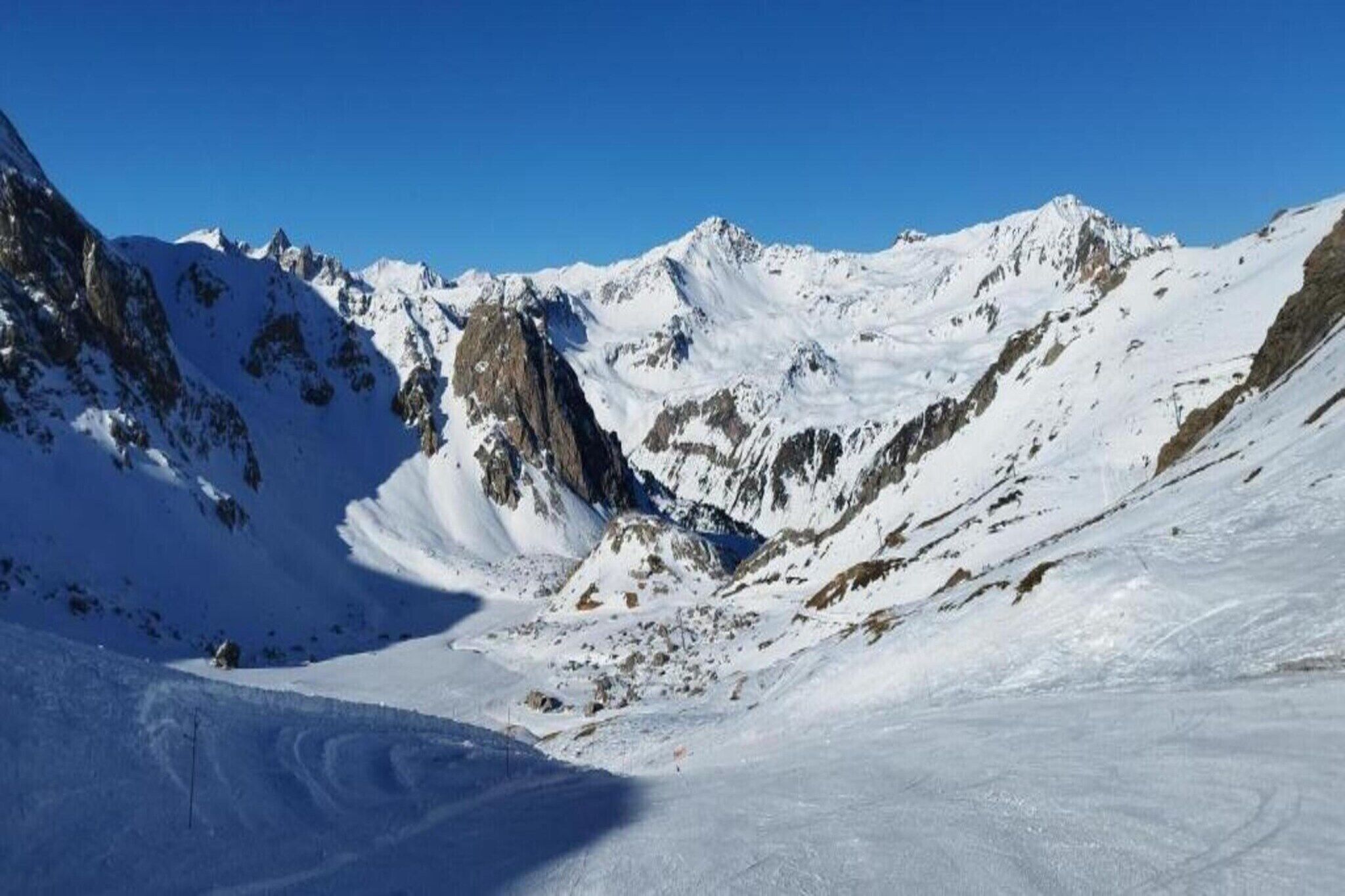 Eine verschneite Berglandschaft mit zerklüftetem Gelände und blauem Himmel.