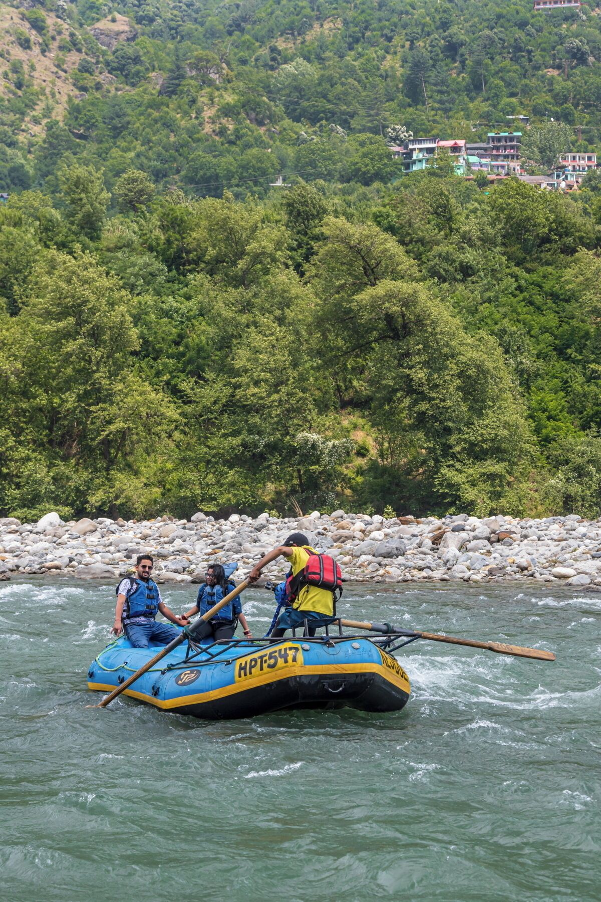 Een groep mensen in een blauwe opblaasboot op een rivier, omringd door een rotsachtige oever en weelderige begroeiing.