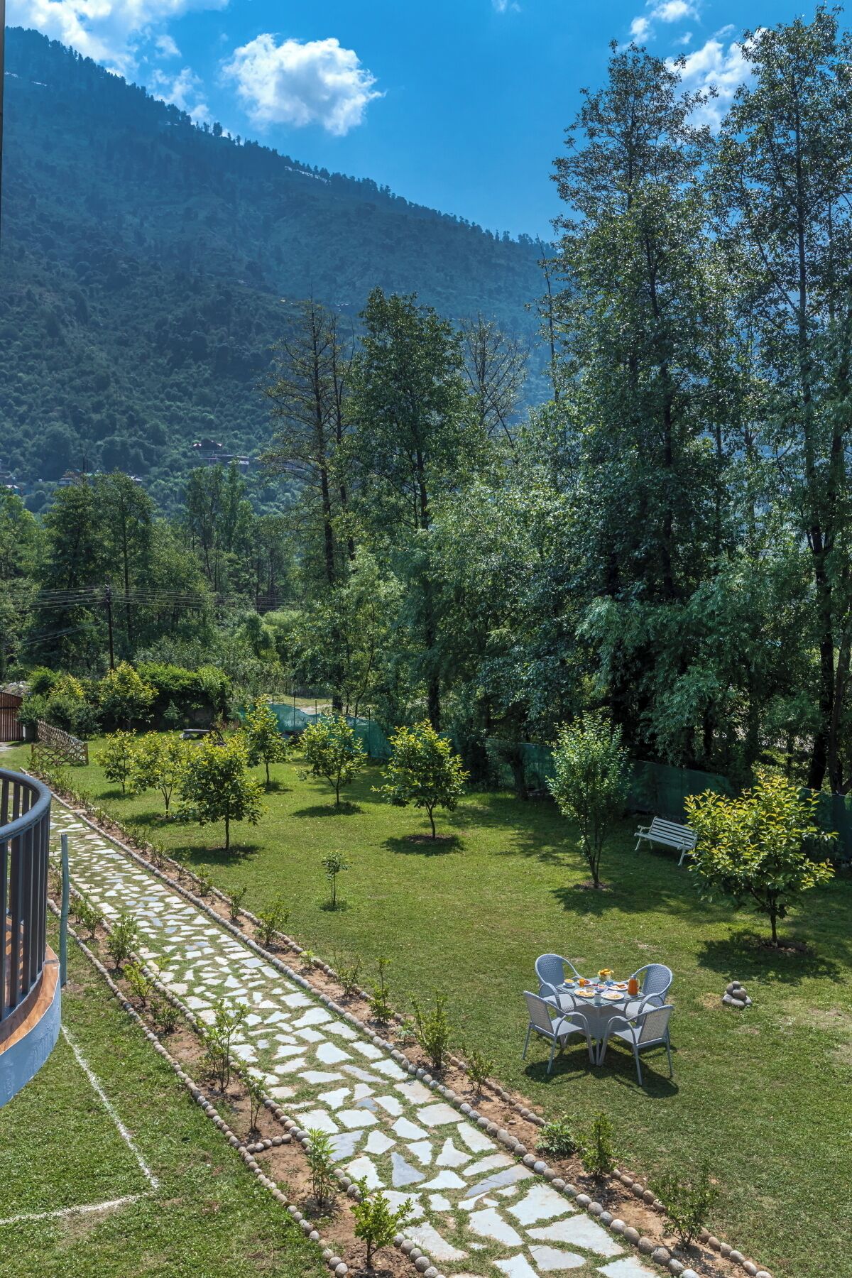 Un jardin avec un sentier en pierre, une table et des chaises, et une vue sur un paysage montagneux.
