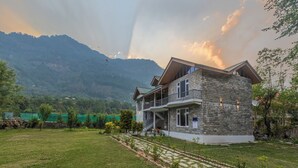 A two-story stone building with a balcony, surrounded by a well-maintained lawn and a mountain backdrop.