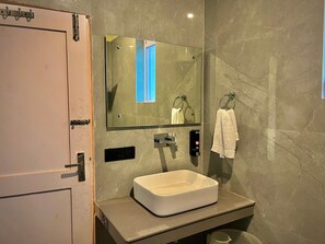 A bathroom with a rectangular sink, a mirror, a towel rack, and a door. - Raison Meadows (Kullu)