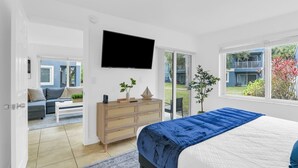 Un dormitorio moderno con una cama grande, un televisor de pantalla plana, un aparador de madera y una puerta corrediza de vidrio que da a un balcón.