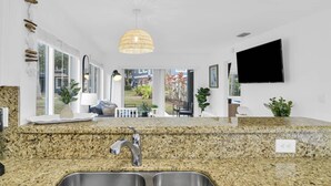 Una cocina moderna con encimeras de granito, un lavabo de acero inoxidable, una lámpara colgante y un amplio ventanal con vistas al exterior.