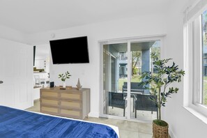 A bedroom with a bed, a dresser, a TV, and a sliding glass door leading to a balcony with outdoor furniture. - 270A - Boca Retreat w/ Pool, Parking, Near Evert Tennis & Shops (Boca Raton)