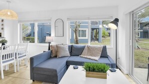 Una sala de estar moderna con un sofá seccional, una mesa de comedor con sillas y ventanas amplias que ofrecen vistas al exterior.